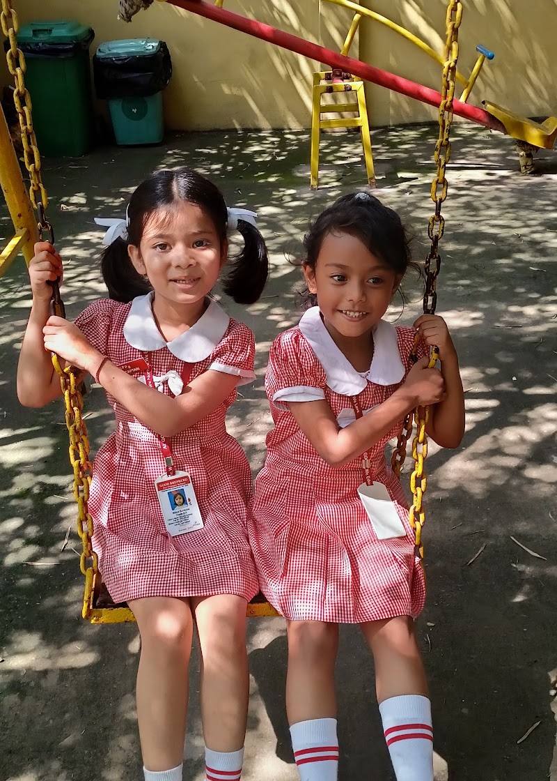 Two smiling girls in pink school uniforms sitting together on a swing at Good Shepherd Pre Primary School, Guwahati